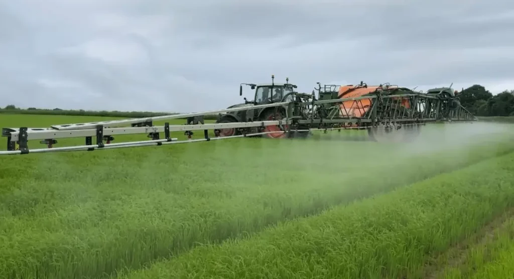 Un tracteur pulvérise du biostimulant sur un champ de lin
