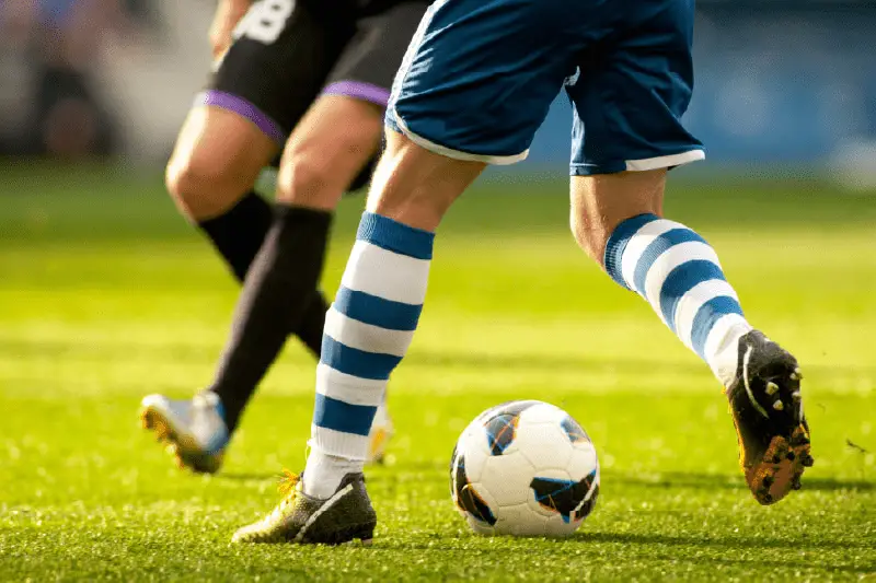 Joueur de football en mouvement sur un gazon sportif dense et bien entretenu, illustrant la résistance du terrain face au piétinement intensif.